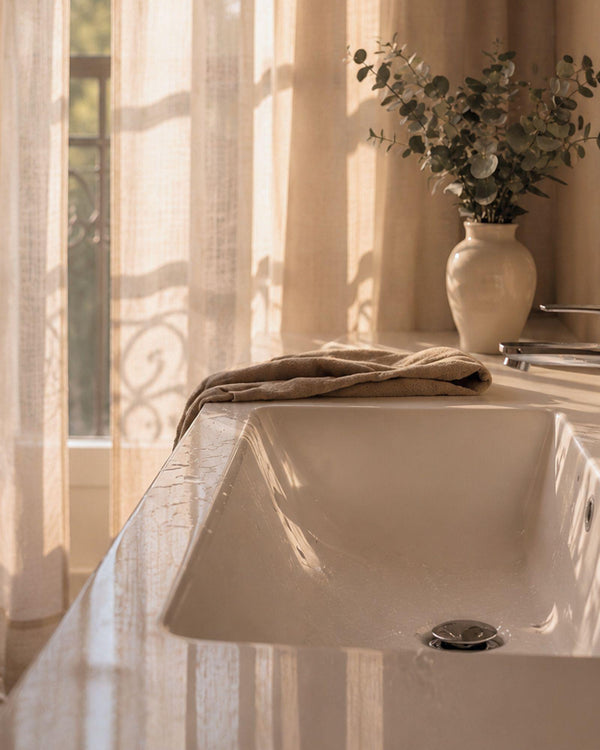 Lavabo blanc dans une salle de bain baignée de lumière naturelle.