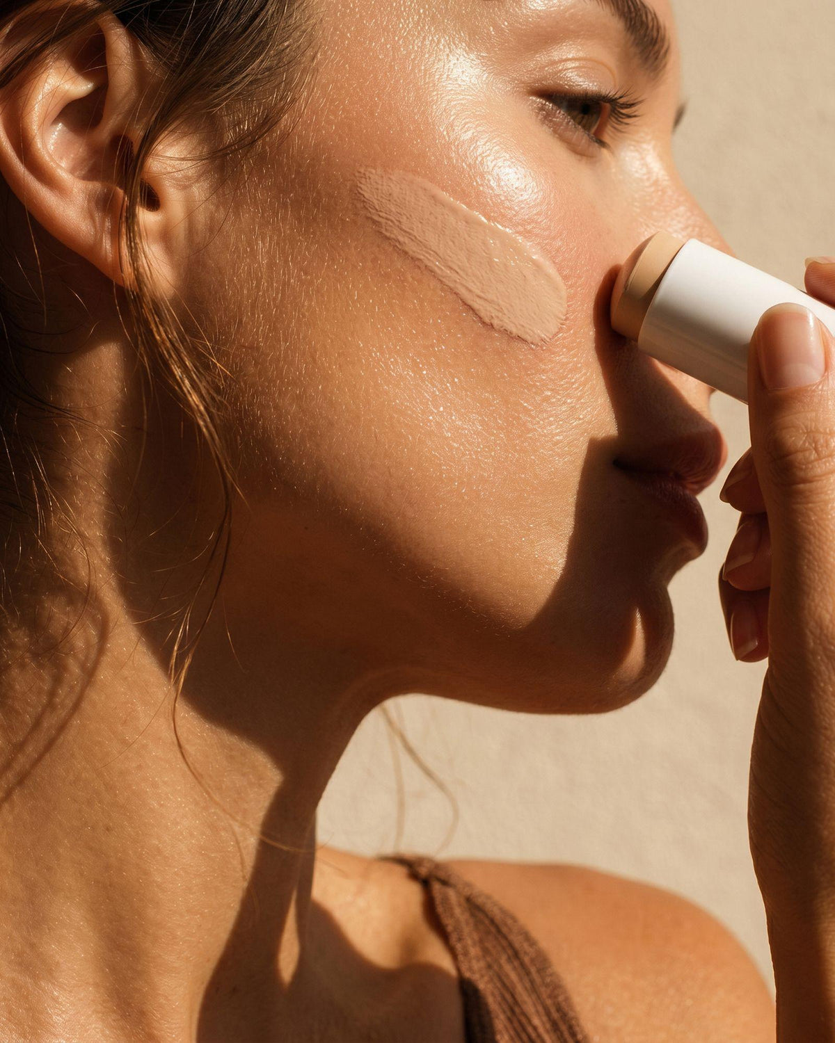 Femme appliquant le stick solaire SPF 50 Voile Protecteur sur sa joue.