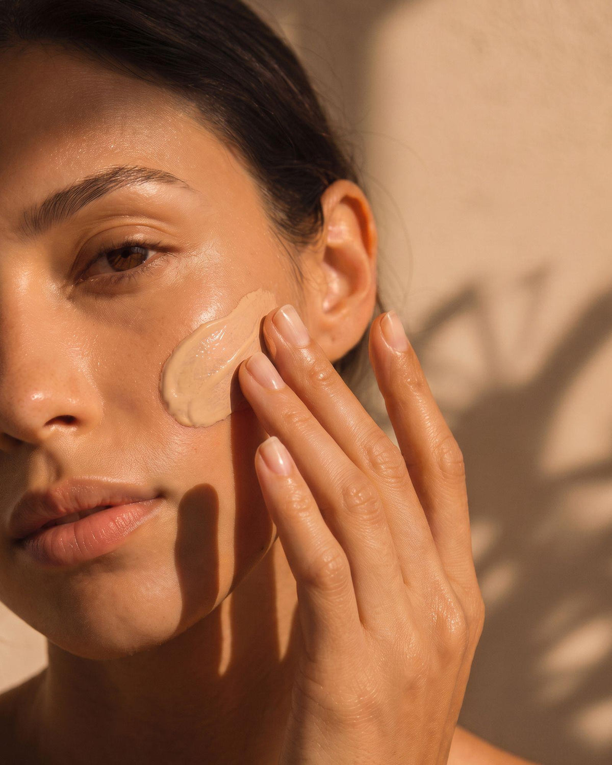 Femme appliquant la crème solaire teintée SPF 30 Voile Teinté sur sa joue.